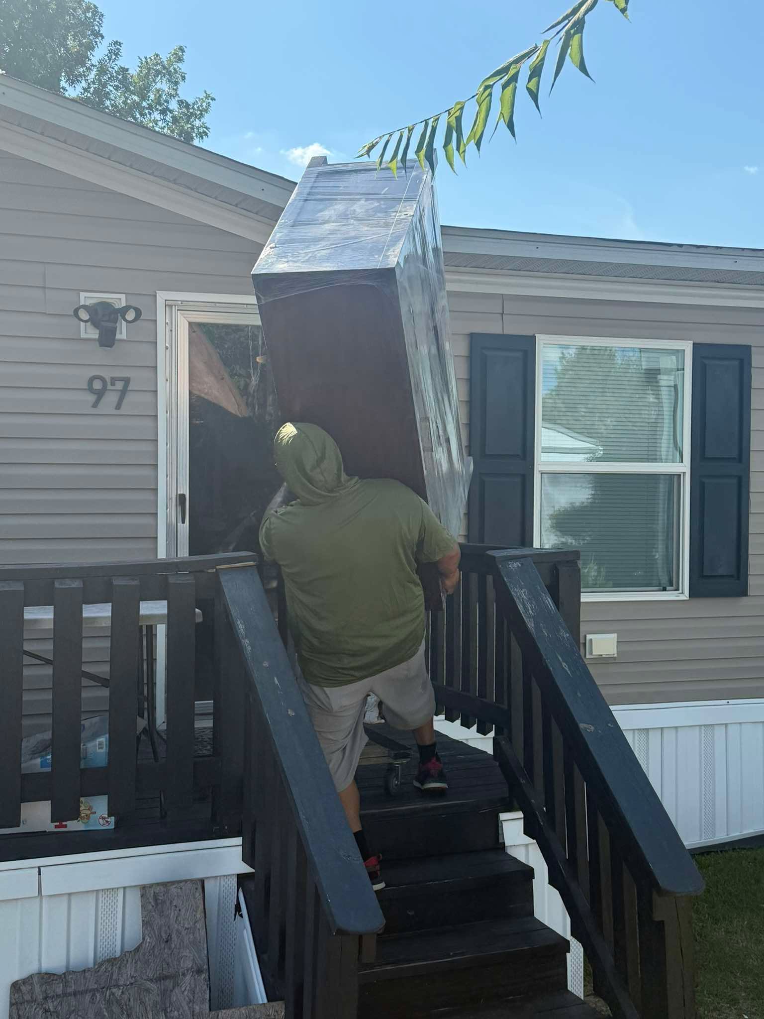 Crew carrying a wrapped cabinet up porch stairs
